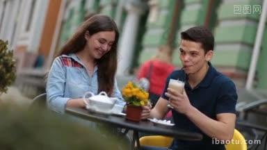一对微笑的情侣坐在户外咖啡馆的桌子旁，谈笑风生的浪漫情侣享受着闲暇时光